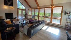A spacious living room with a fireplace, large windows, and a wooden ceiling. - Beautiful cottage w/firepit, pool and a river in the property (Duclos)