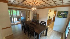 A dining area with a large wooden table and chairs, a chandelier, and a painting of a lotus on the wall. - Beautiful cottage w/firepit, pool and a river in the property (Duclos)