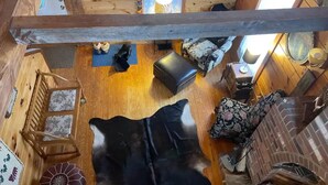 Ein gemütliches Blockhaus-Interieur mit Holzboden, einem großen schwarz-weißen Teppich, einer Holztreppe, einer Couch, einem kleinen Tisch und einem Kamin.