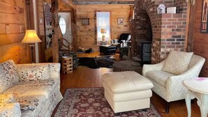 Ein gemütliches Blockhaus-Interieur mit Kamin, Holzwänden, einer Couch, einem Sessel und einem kleinen Tisch.