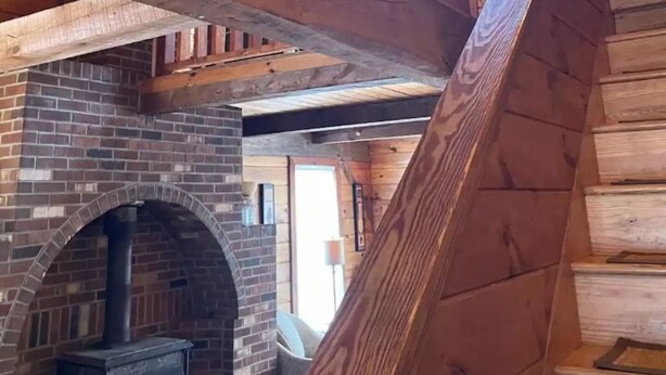 Ein Holzinnenraum mit Kamin aus Ziegelsteinen, einer Holztreppe und einem Deckenventilator.