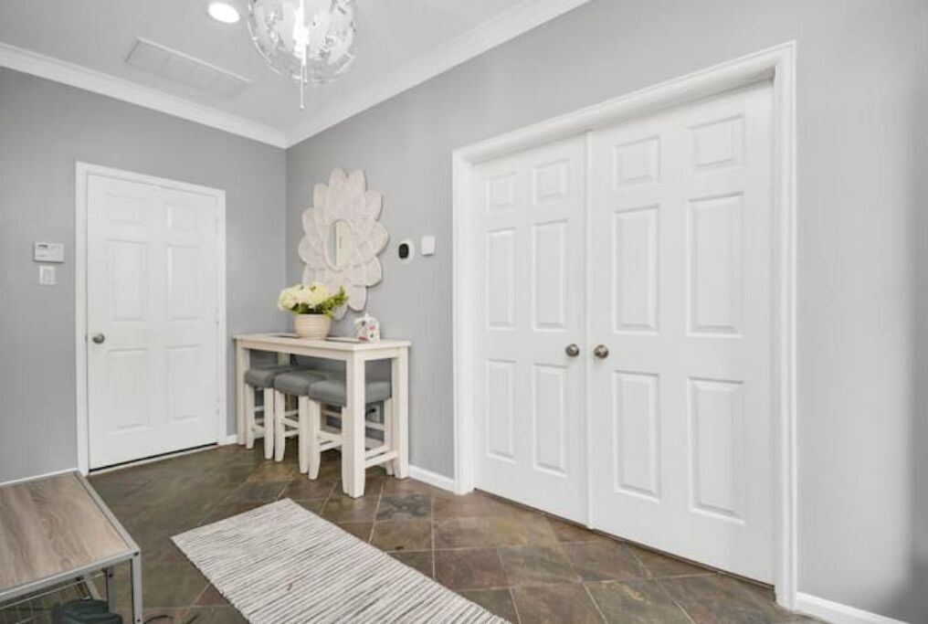 A hallway with a white door, a small table with a vase of flowers, and a rug on the floor.