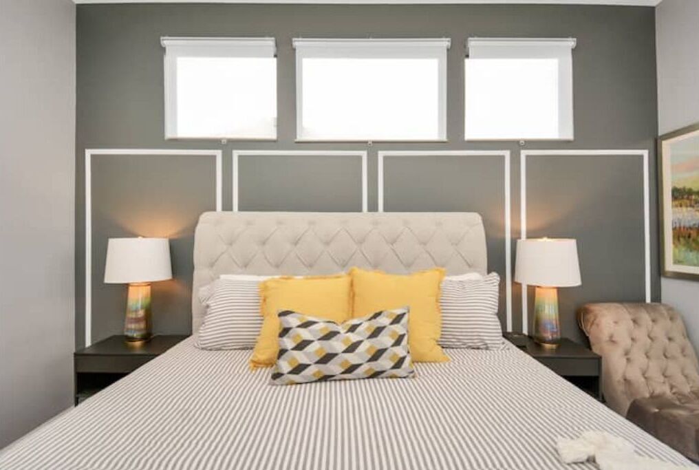 Une chambre à coucher avec une tête de lit capitonnée, une couvre-lit à rayures et deux lampes de chevet.