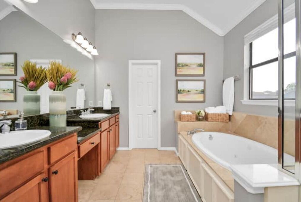 A modern bathroom with a large bathtub, double sinks, wooden cabinets, and framed artwork on the walls.
