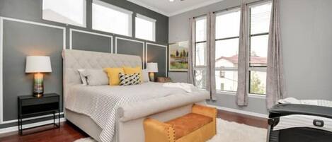 A bedroom with a large bed, a ceiling fan, a window with curtains, and a white rug.