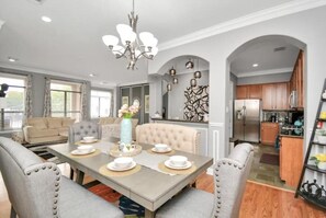 A dining area with a table set for four, a chandelier, and a view into the kitchen. - Modern | Luxe | 3BR/3.5Ba Spacious Home | Walkable (Houston)