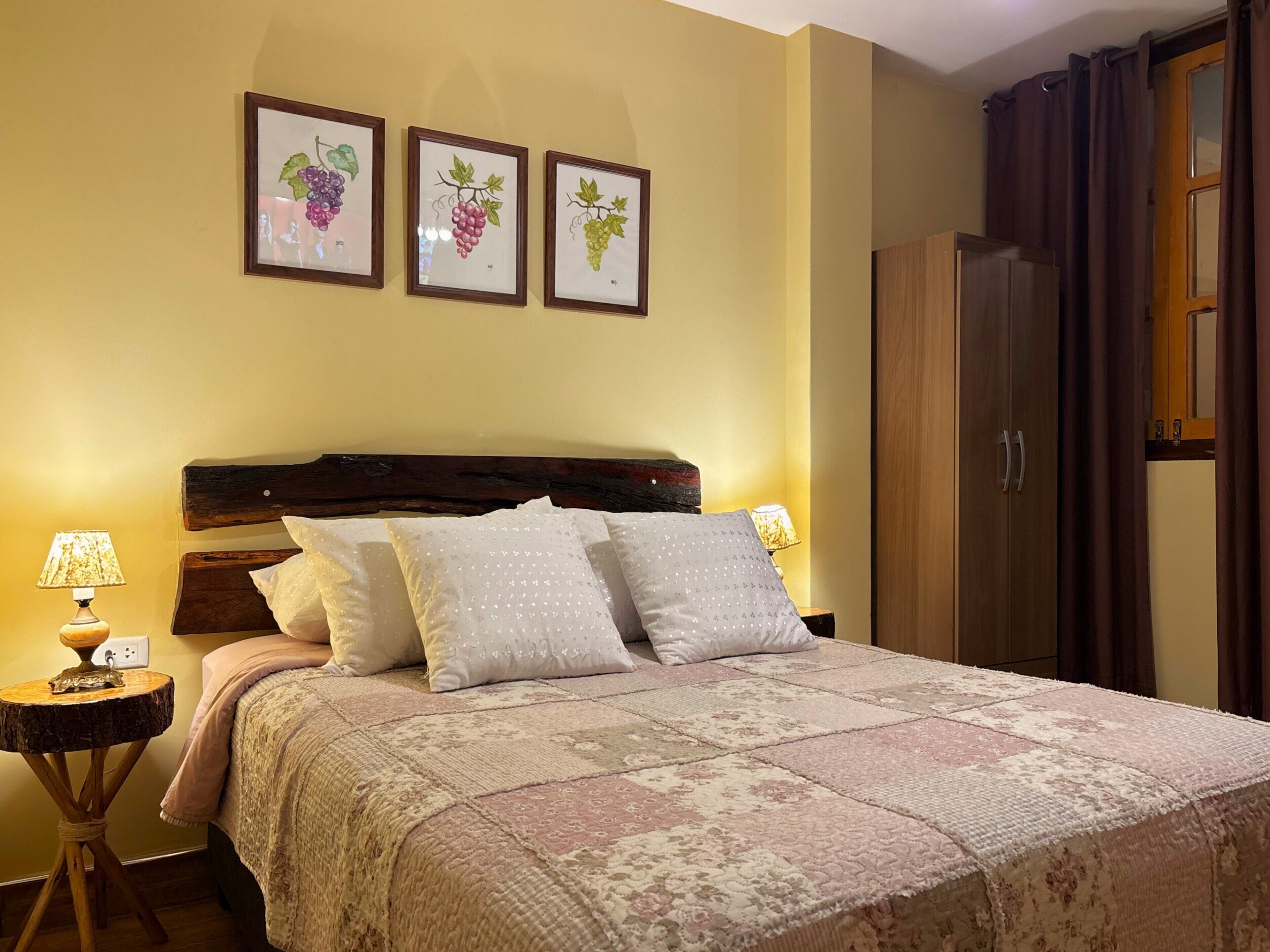 A bedroom with a wooden headboard, a large bed with patterned bedding, a nightstand with a lamp, and a wardrobe.