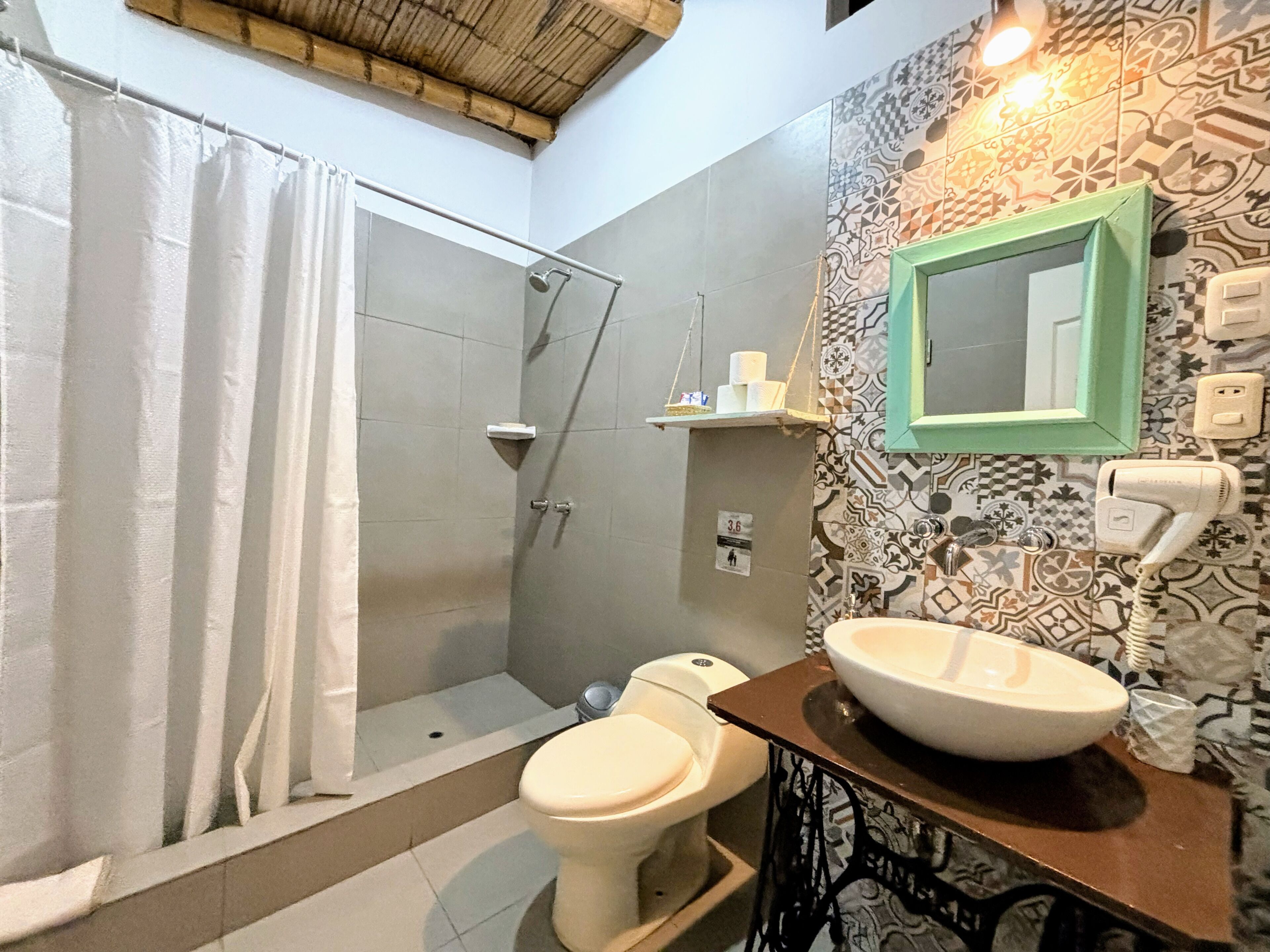 A bathroom with a shower, toilet, sink, and a mirror with a green frame.