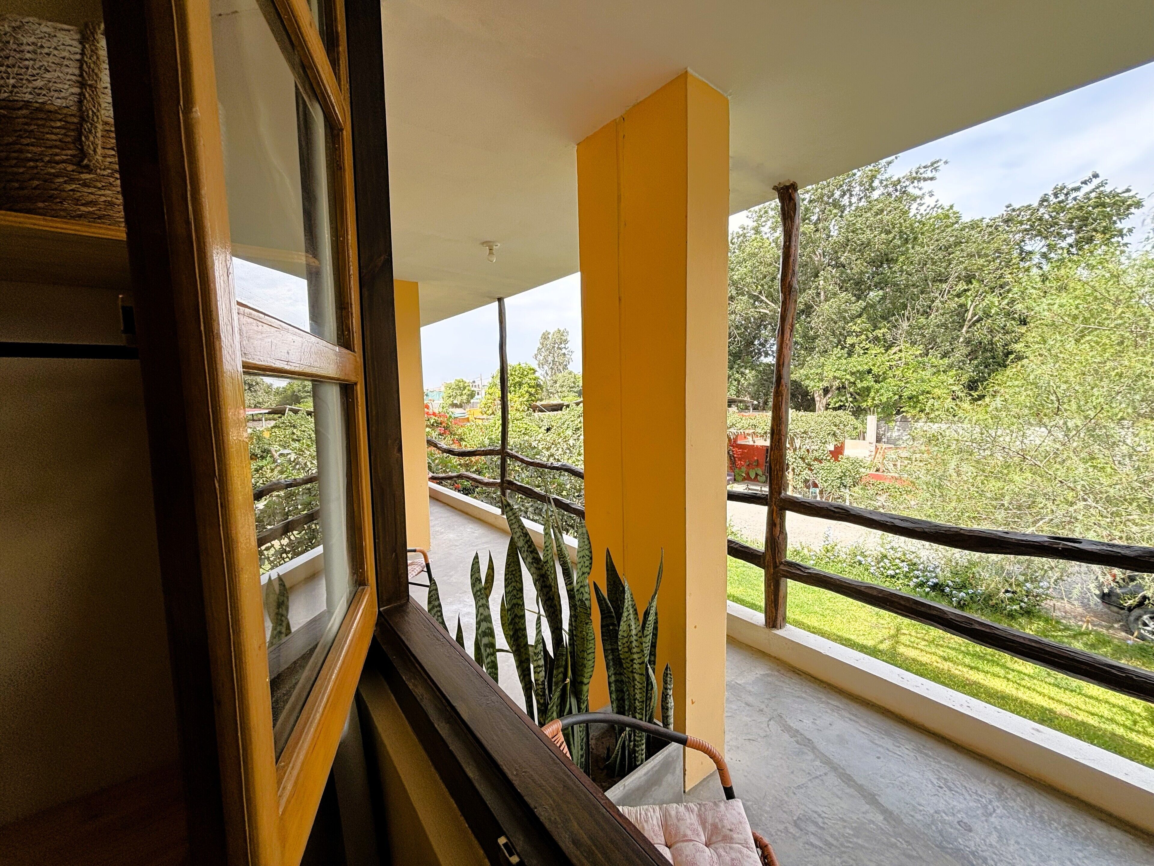 A balcony with yellow pillars, a view of greenery and trees, and a chair.