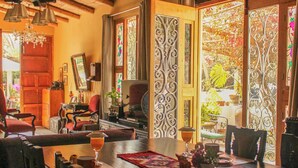 A cozy dining area with a wooden table, chairs, and a chandelier. There are decorative items on the table and a view of the outdoors through a glass door. - Serenity Lodge (Ica)