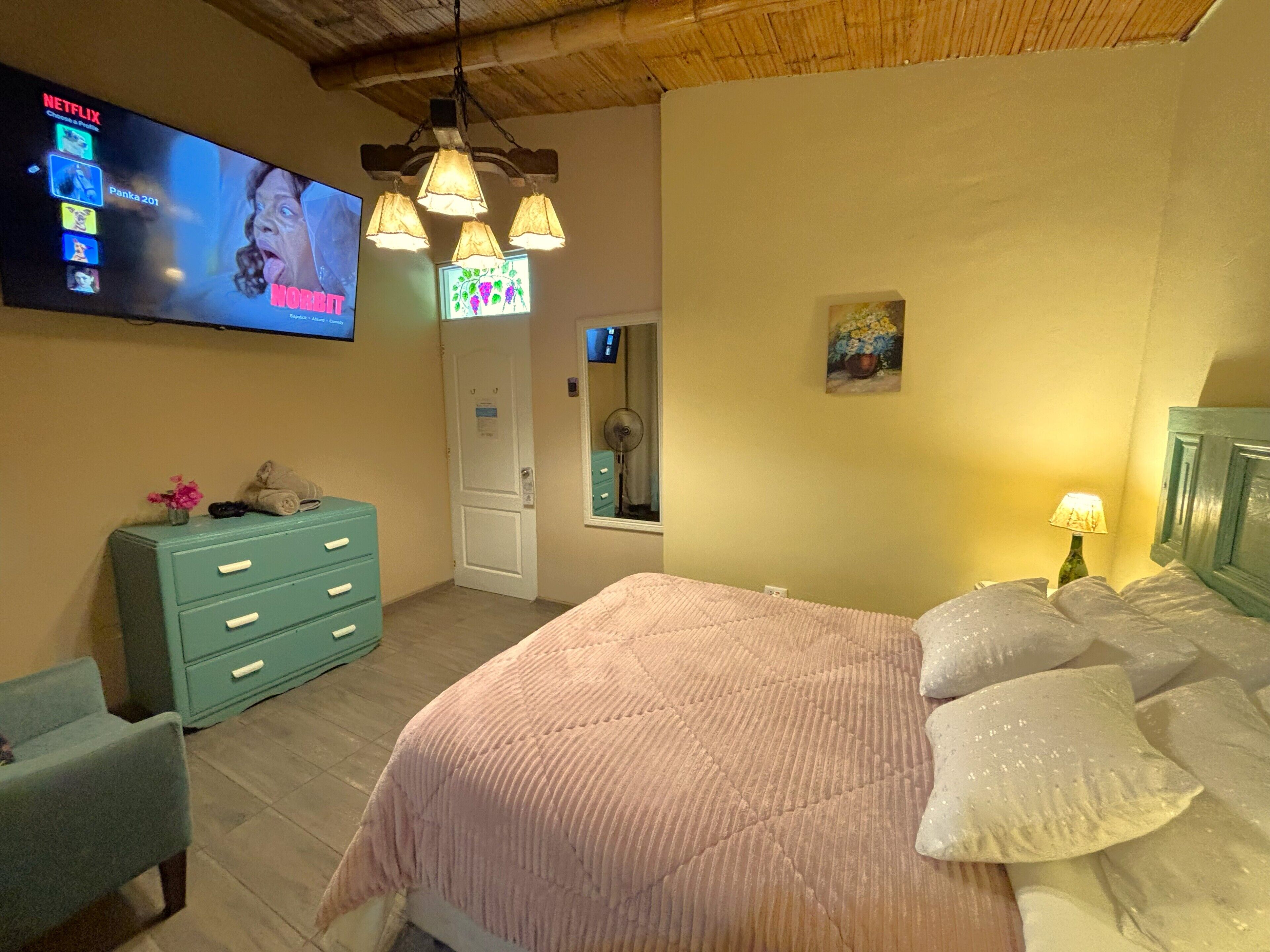 A bedroom with a bed, a dresser, a TV mounted on the wall, and a ceiling fan.