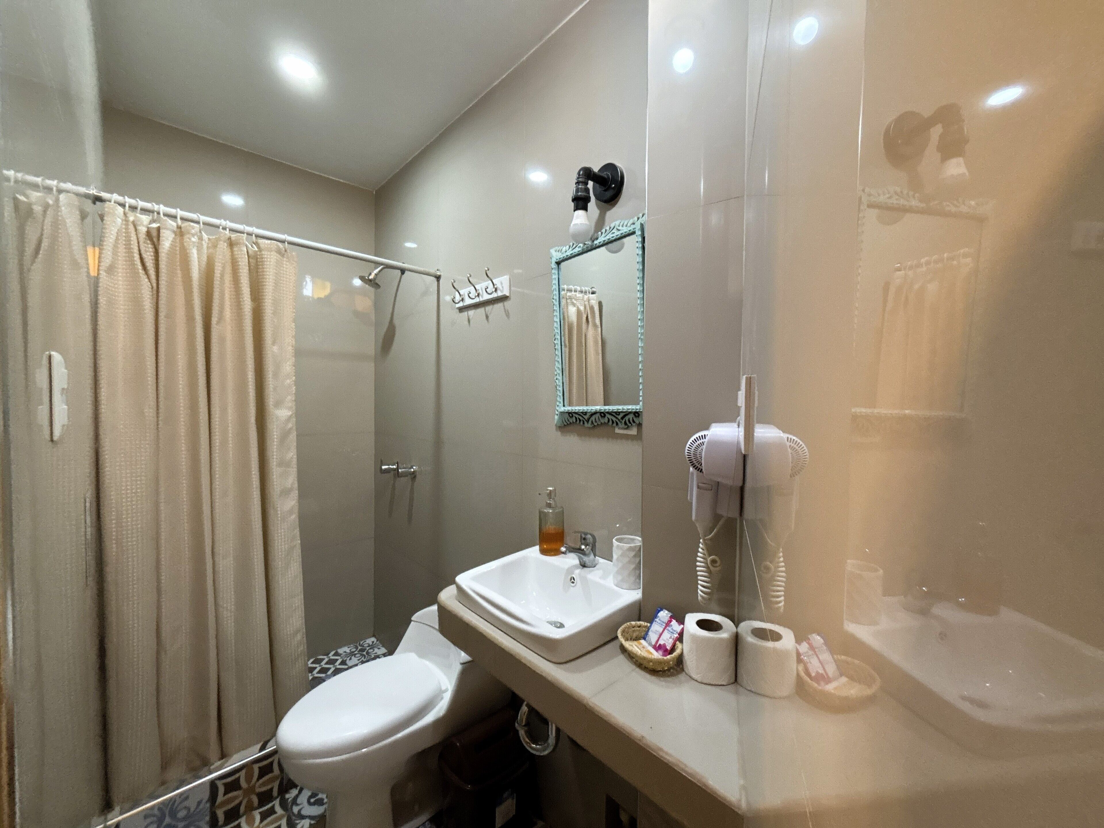 A modern bathroom with a glass shower enclosure, a toilet, a sink with toiletries, and a hairdryer.