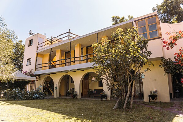 A two-story building with a balcony, arched doorways, and a garden area with potted plants and a tree. - Serenity Lodge (Ica)