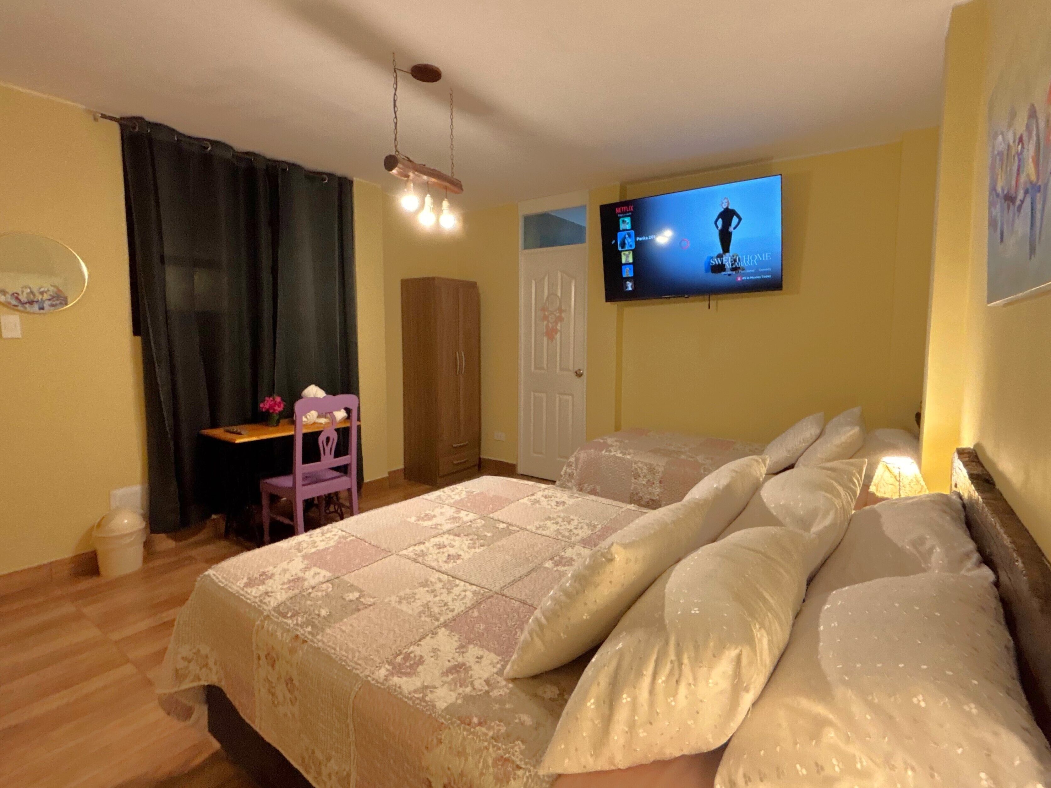 Un dormitorio con una cama, un escritorio, una silla, un armario y un televisor en la pared.
