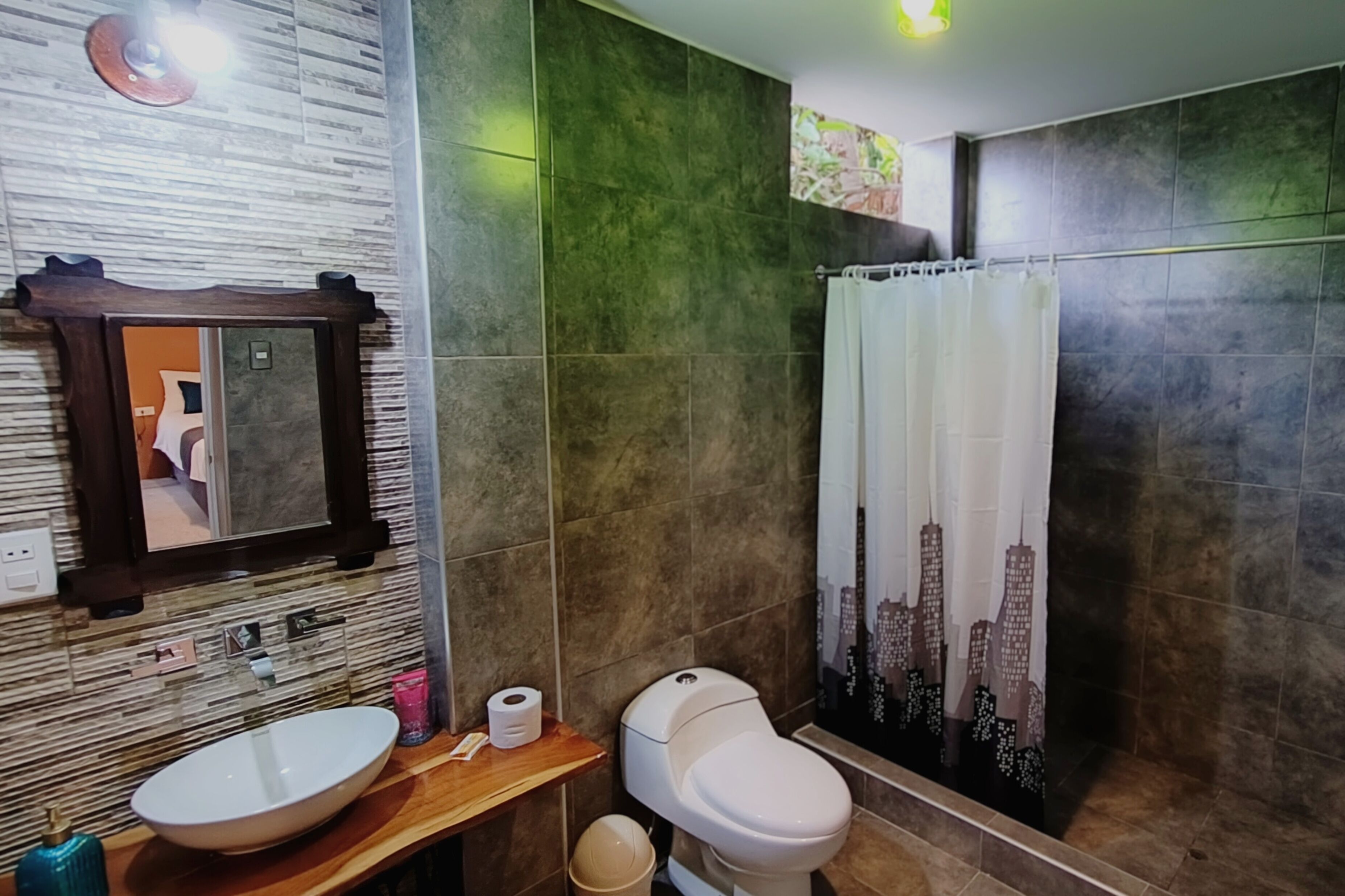 A bathroom with a wooden vanity, a white sink, a toilet, and a shower curtain with a cityscape design.