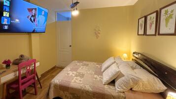 A bedroom with a bed, a desk, a chair, a TV, and wall art.