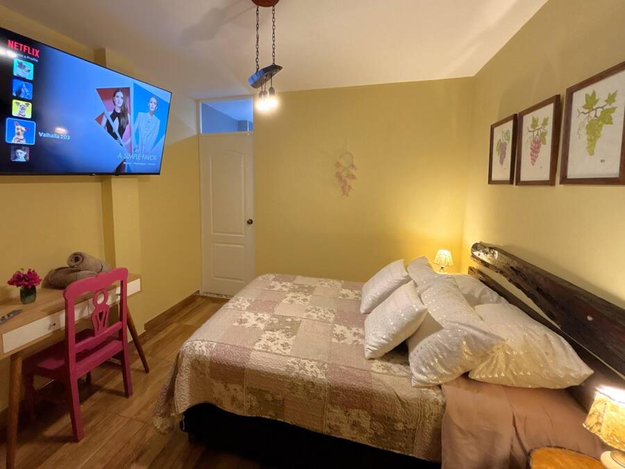 A bedroom with a bed, a desk, a chair, a TV, and wall art.