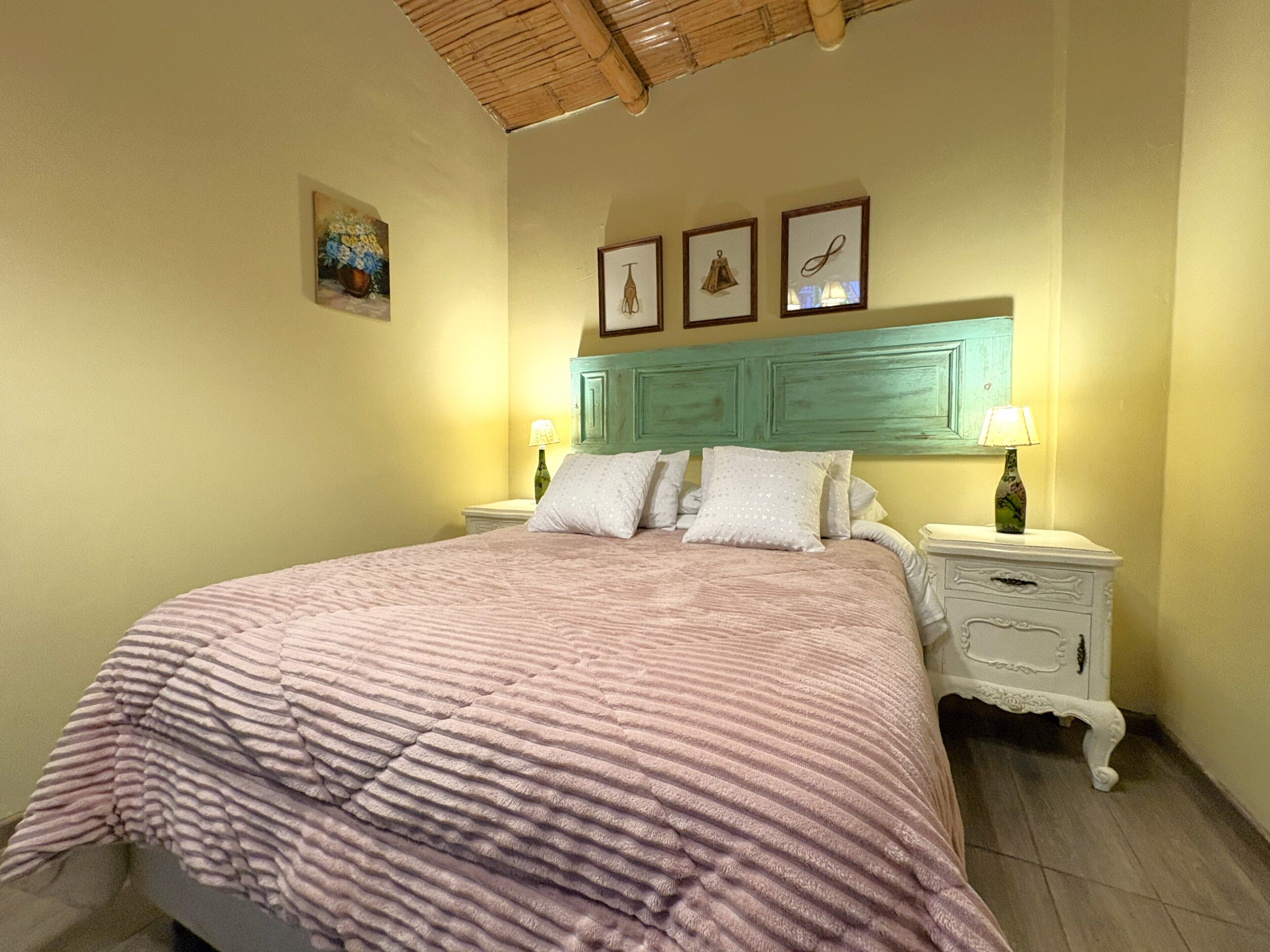 A bedroom with a bed, two bedside tables, a nightstand, a headboard, and wall-mounted pictures.