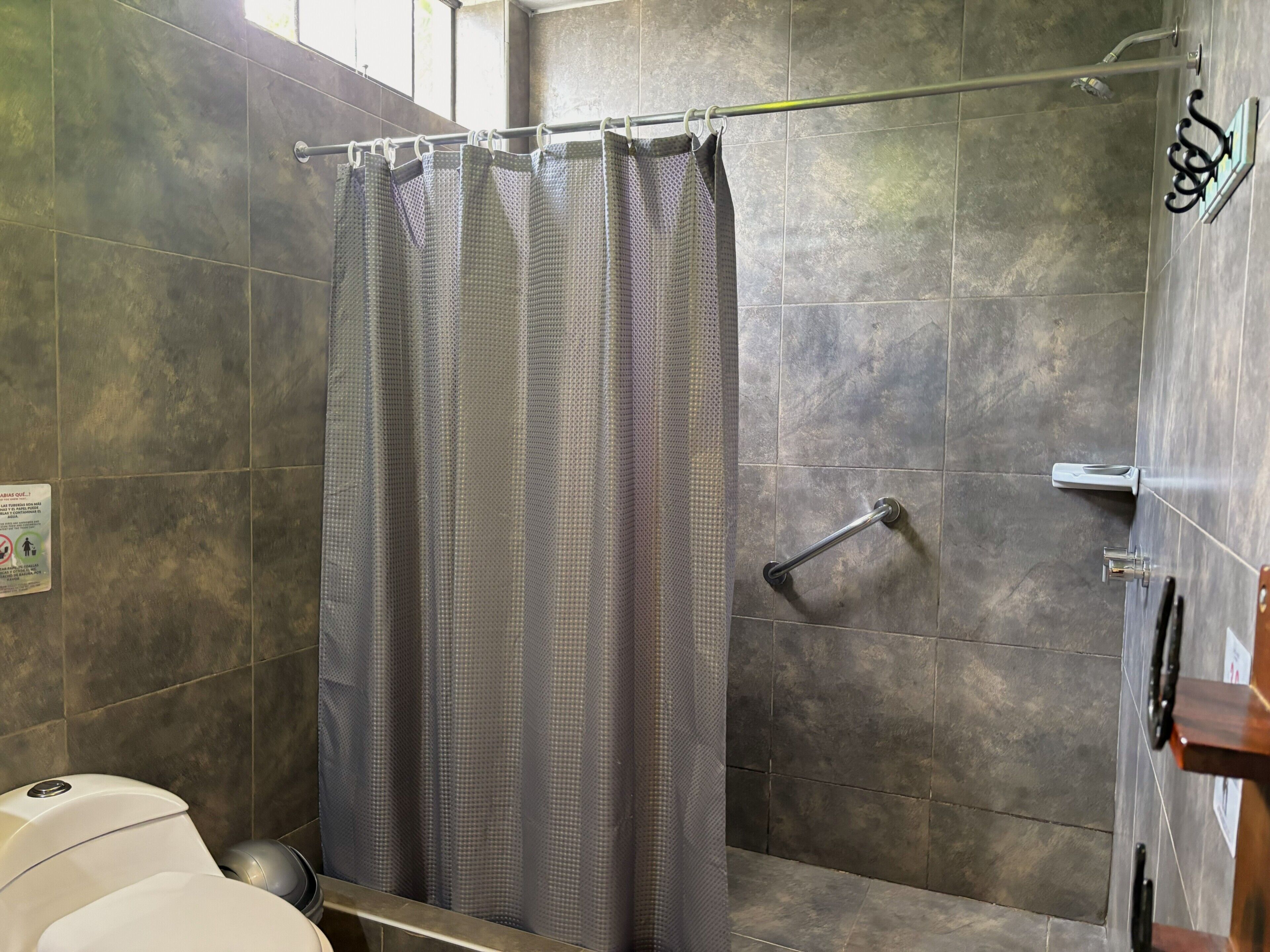 Un baño con cortina de ducha, barra de apoyo y retrete.