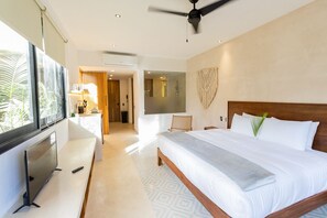 Une chambre d’hôtel moderne dotée d’un grand lit, d’une télévision, d’un ventilateur de plafond et offrant une vue sur les palmiers.