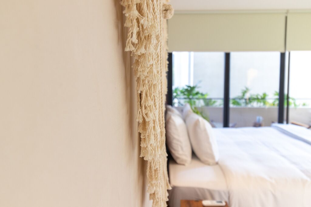 A bedroom with a bed, pillows, and a macramé curtain.