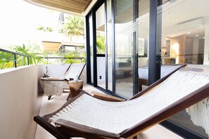 A balcony with a hammock, a macrame chair, and a small table with a plant.