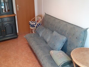 Um quarto com um sofá cinzento, uma mesa redonda pequena e um armário de madeira.