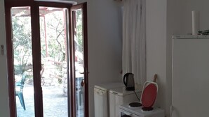 A compact kitchen with a refrigerator, a microwave, and a kettle. There is a sliding glass door leading to an outdoor area with a stone floor and a green chair. - Apartments Rudi - Superior One bedroom Apartment with Terrace and Sea View (Klenovica)