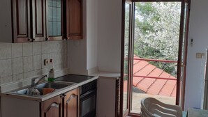A kitchen with wooden cabinets, a dishwasher, and a view of a red-roofed building through a sliding glass door. - Apartments Rudi - One Bedroom Apartmen with Terrace and Sea View (Klenovica)