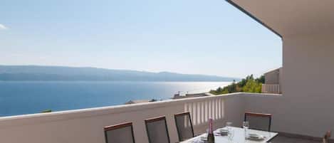A dining table set for four on a balcony with a view of the sea and distant mountains.