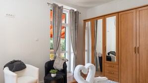 Een hotelkamer met een bed, een kledingkast, een stoel, een klein tafeltje met een plant en een raam met gordijnen.