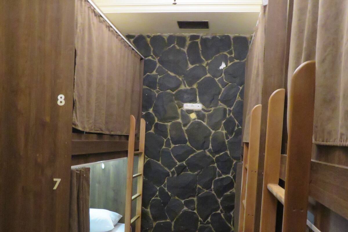 A small, narrow room with bunk beds, a stone wall, and a tiled floor.