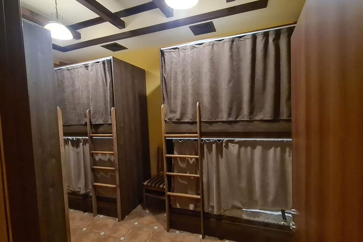 A dormitory room with bunk beds, wooden ladders, and curtains.