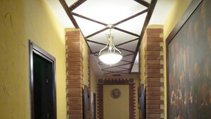 A hallway with a tiled floor, a ceiling with a geometric pattern, and a chandelier. There is a door on the left and a framed picture on the right. - Hotel Jan-Hostel Jan (Yerevan)