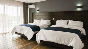 Habitación de hotel con dos camas, un ventanal grande con cortinas y un aire acondicionado en la pared.