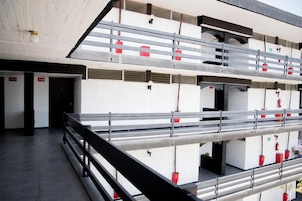 Un edificio de varios pisos con balcones, habitaciones numeradas y macetas rojas.