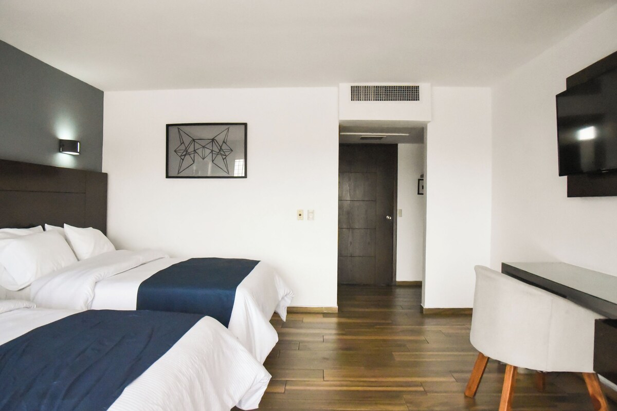 Una habitación de hotel moderna con dos camas, un escritorio, un televisor de pantalla plana y una obra de arte abstracta enmarcada en la pared.