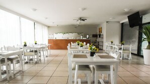 Un comedor espacioso con mesas y sillas blancas, una barra central y un ventilador de techo.