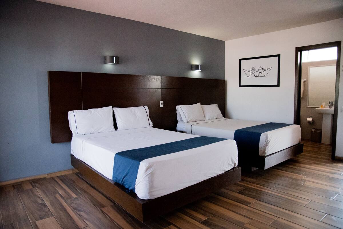 Une chambre d’hôtel avec deux lits, un plancher en bois, une tête de lit sombre et une œuvre d’art encadrée au mur.