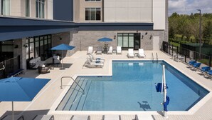 Ein Dachpool mit Liegestühlen und Sonnenschirmen, umgeben von einem Gebäude mit großen Fenstern und einer Stein-Fassade.