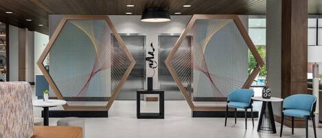 Un vestíbulo moderno con un diseño geométrico en la pared, una pieza de arte central y zonas de descanso.