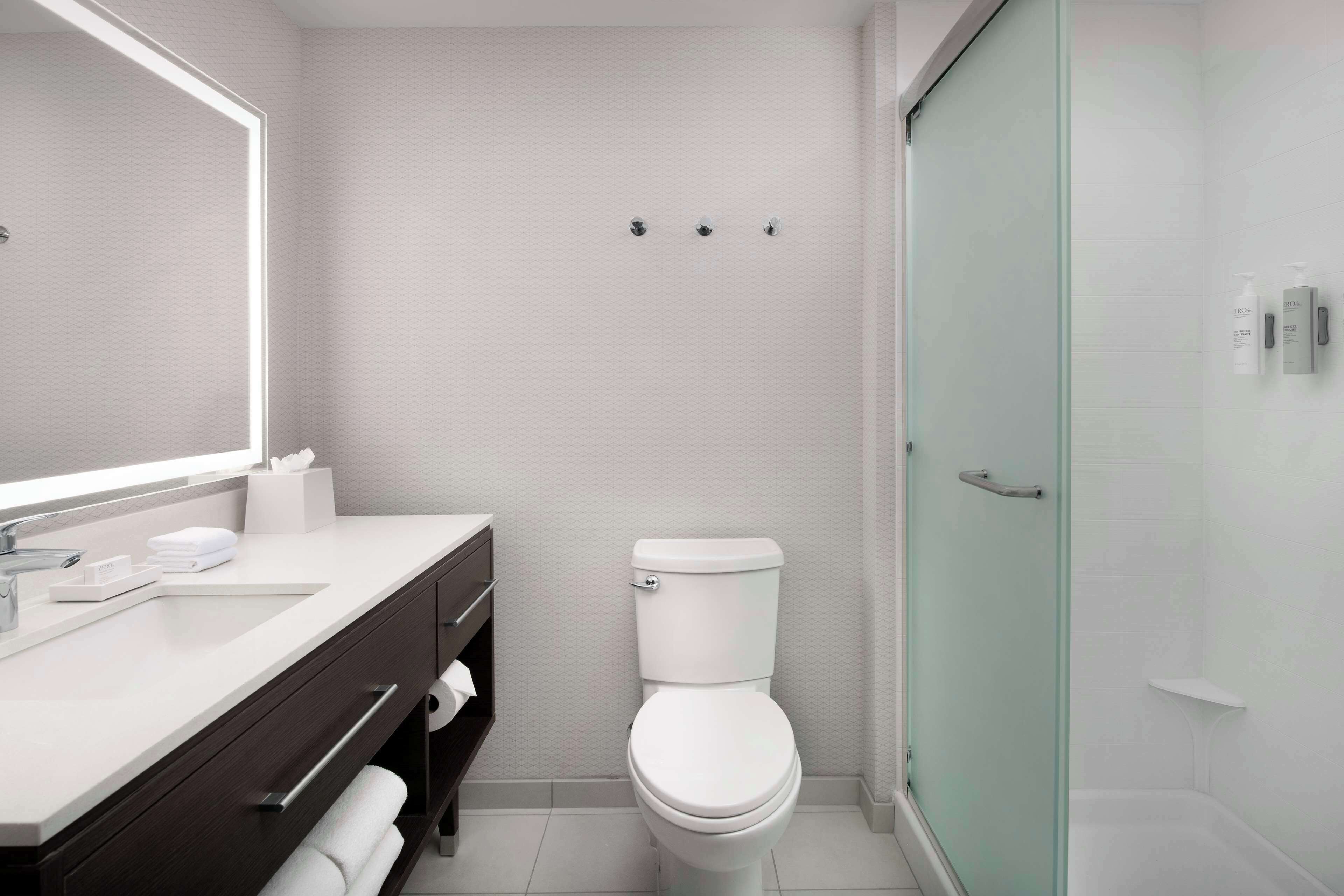 A modern bathroom with a white sink, dark wooden vanity, a toilet, and a glass shower enclosure.