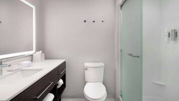 A modern bathroom with a white sink, dark wooden vanity, a toilet, and a glass shower enclosure.