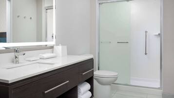 A modern bathroom with a large mirror, a white sink, dark wooden vanity, a toilet, and a glass-enclosed shower.