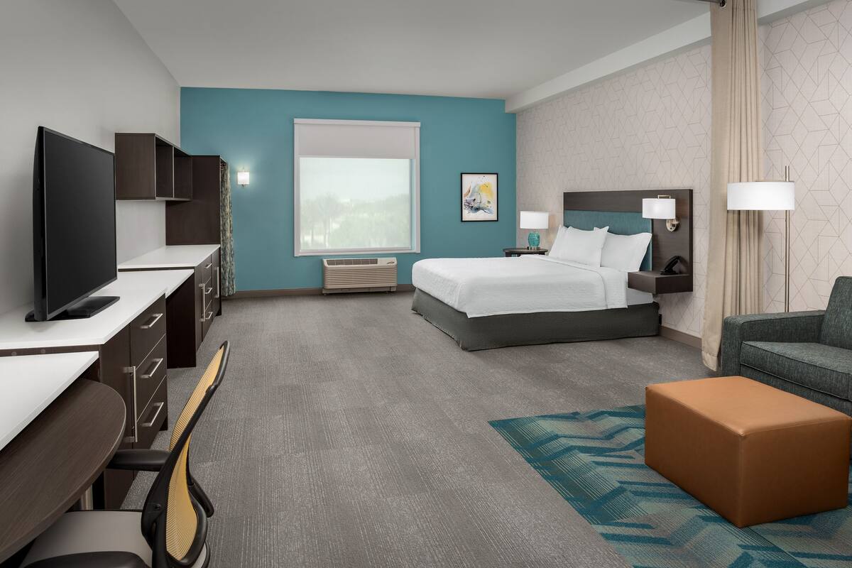 Een hotelkamer met een bed, bureau, televisie en uitzicht op de omgeving.