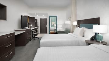 A hotel room with two beds, a desk, a chair, a TV, and a bathroom visible in the background.