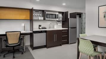 A modern kitchen with a microwave, dishwasher, and refrigerator. There is a dining table with chairs and a small office area with a chair and desk.