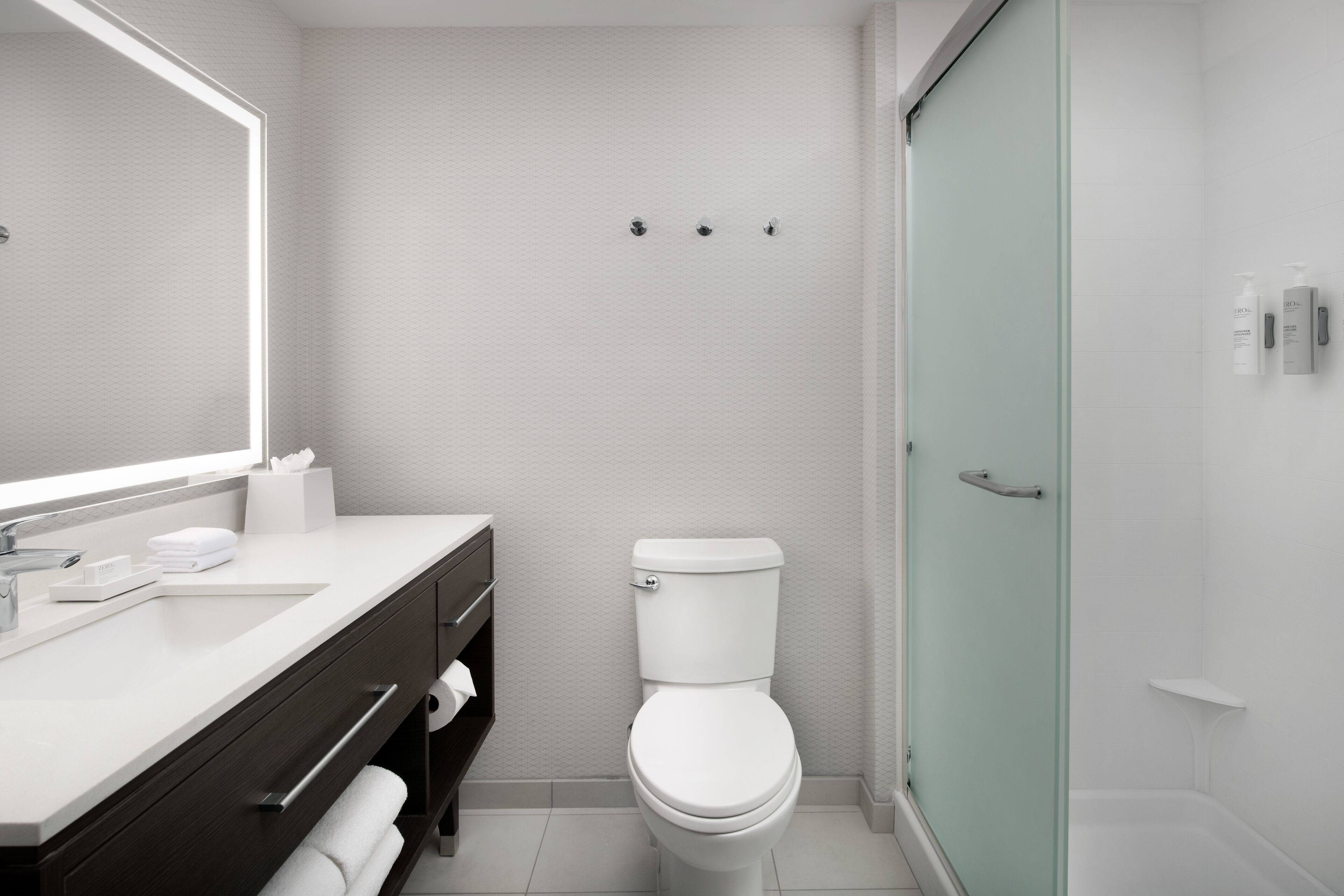A modern bathroom with a white sink, vanity, and toilet. There is a glass shower enclosure to the right.