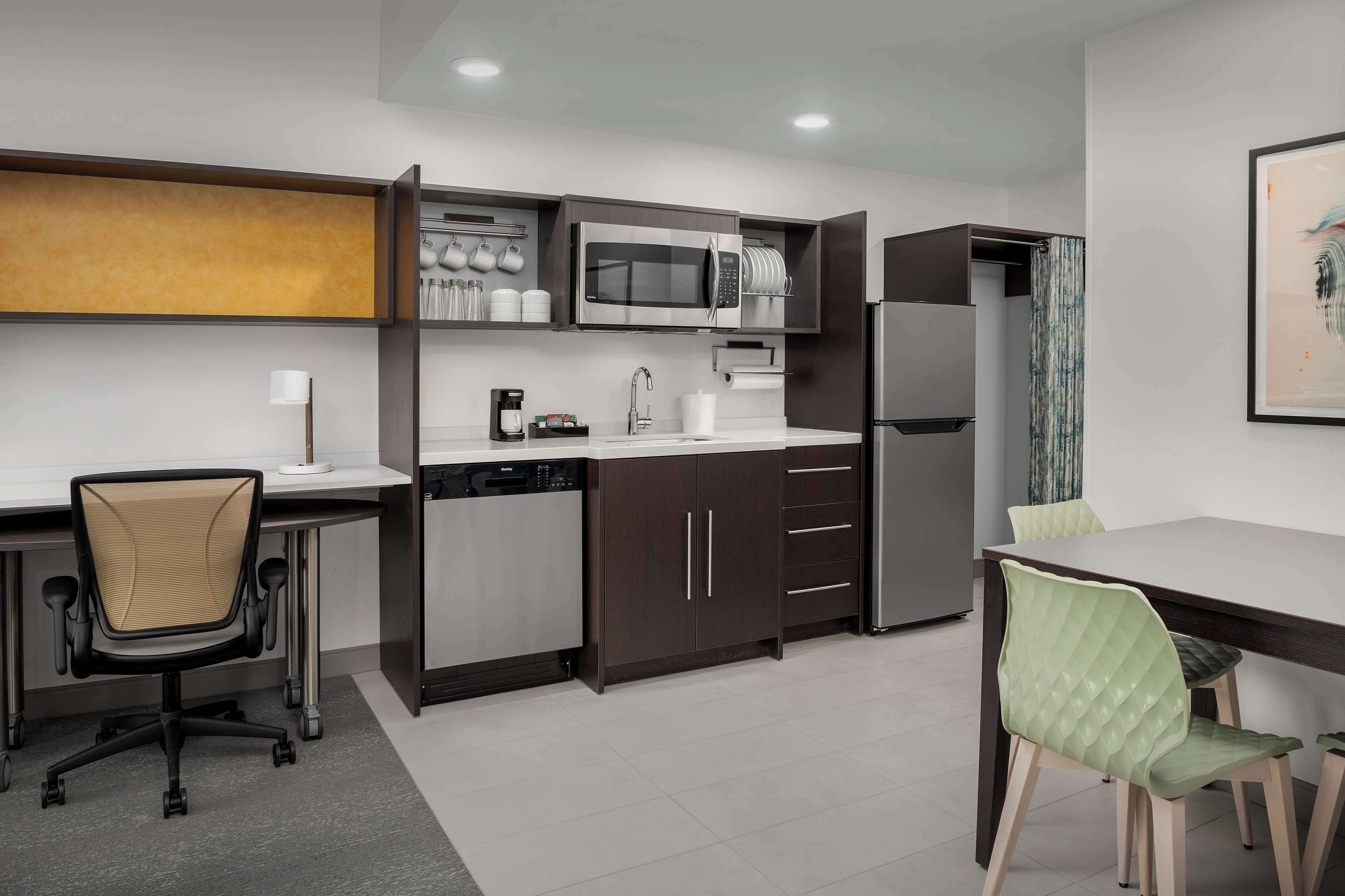 A modern kitchen with a microwave, coffee maker, and dishwasher. There is a dining table with chairs and a small office chair.
