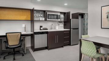 A modern kitchen with a microwave, coffee maker, and dishwasher. There is a dining table with chairs and a small office chair.